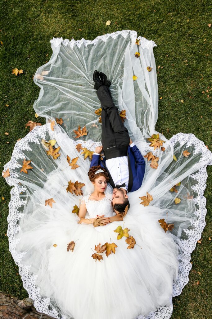 pexels-photo-265722-265722 Bride and groom lying together on a lawn surrounded by autumn leaves, captured from above.